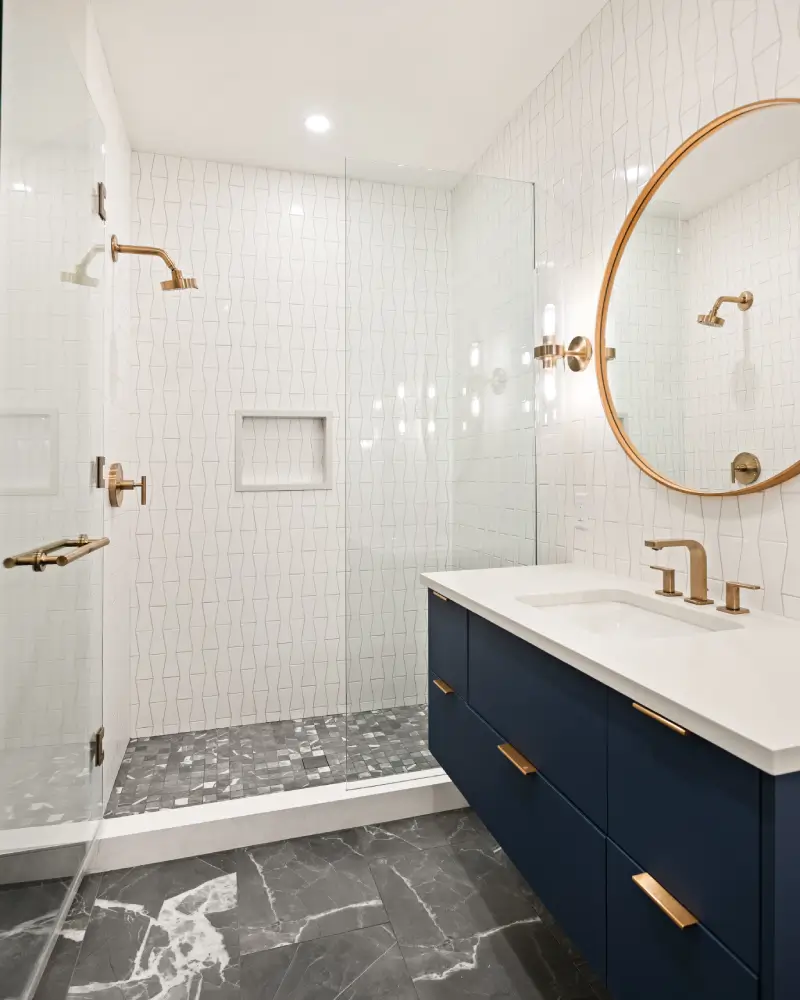 This modern bathroom in Missouri Heights features a sleek dark blue vanity paired with striking brushed gold fixtures and a large circular mirror