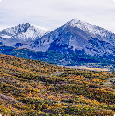 Panoramic view of snow-capped mountains above vibrant autumn foliage