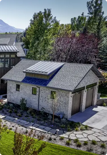 Two-story-stone-garage-with-wood-doors-dark-roof-and-landscaped-yard Two-story stone garage with wood doors, dark roof, and landscaped yard